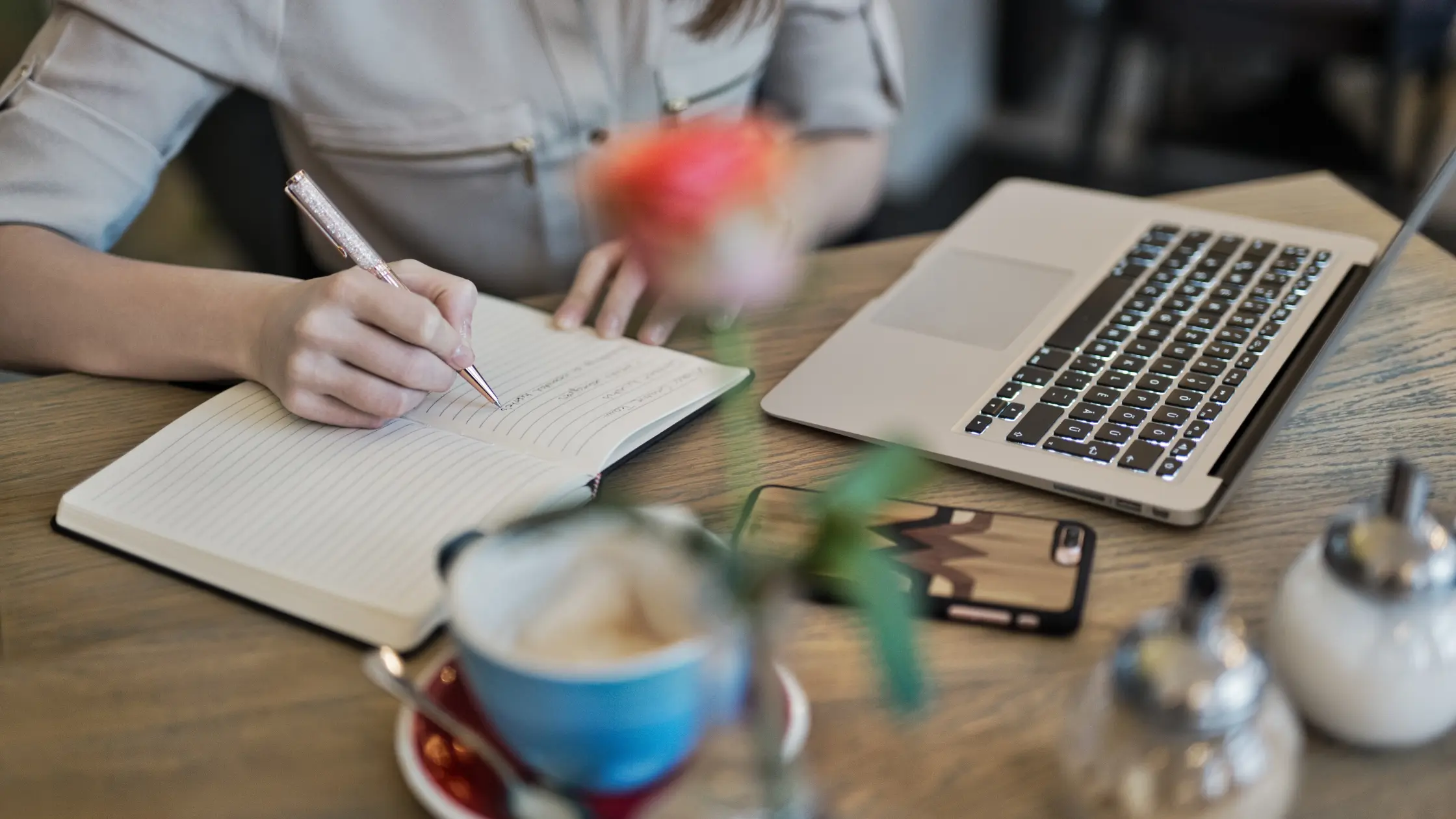 A woman doing content writing with a coffee and a laptop and a phone nearby